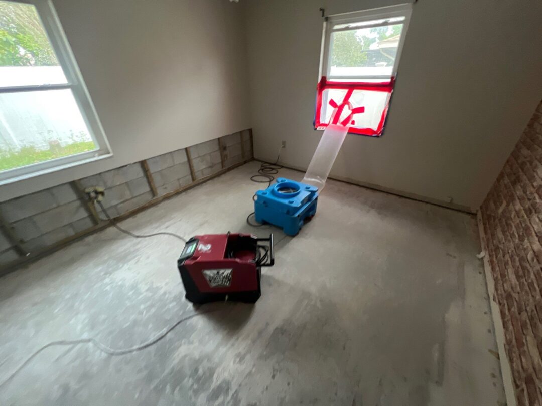 Industrial drying equipment set up in a residential room undergoing post-restoration drying after water damage, with wall sections removed to address mold concerns and a sealed window for moisture control.