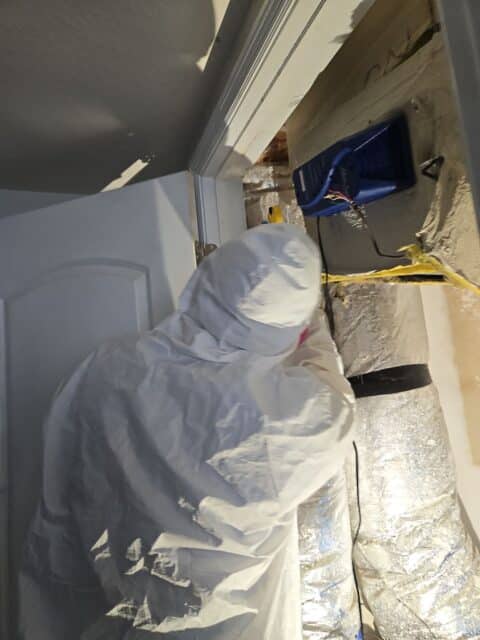 Mold remediation expert in protective suit working near an air duct system, utilizing specialized equipment to remove mold and restore a safe living environment during a mold removal process.