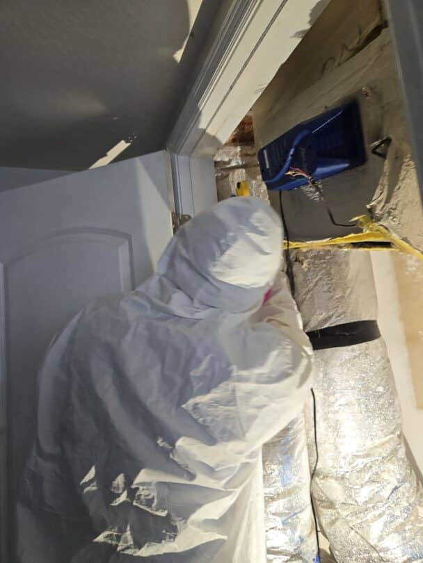 Mold remediation expert in protective suit working near an air duct system, utilizing specialized equipment to remove mold and restore a safe living environment during a mold removal process.