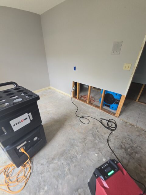 Mold remediation setup in a residential room with drywall removed and professional air scrubbers and drying equipment targeting hidden moisture and potential mold behind walls.