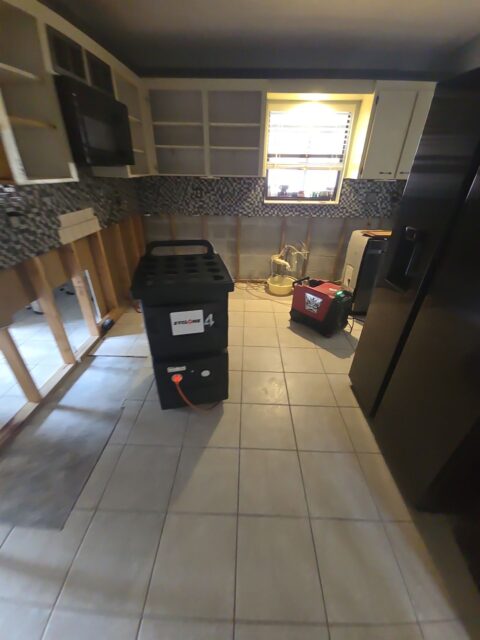 Mold remediation in a residential kitchen with lower drywall removed and industrial air scrubbers and dehumidifiers deployed to eliminate moisture and prevent mold growth behind cabinets and walls.